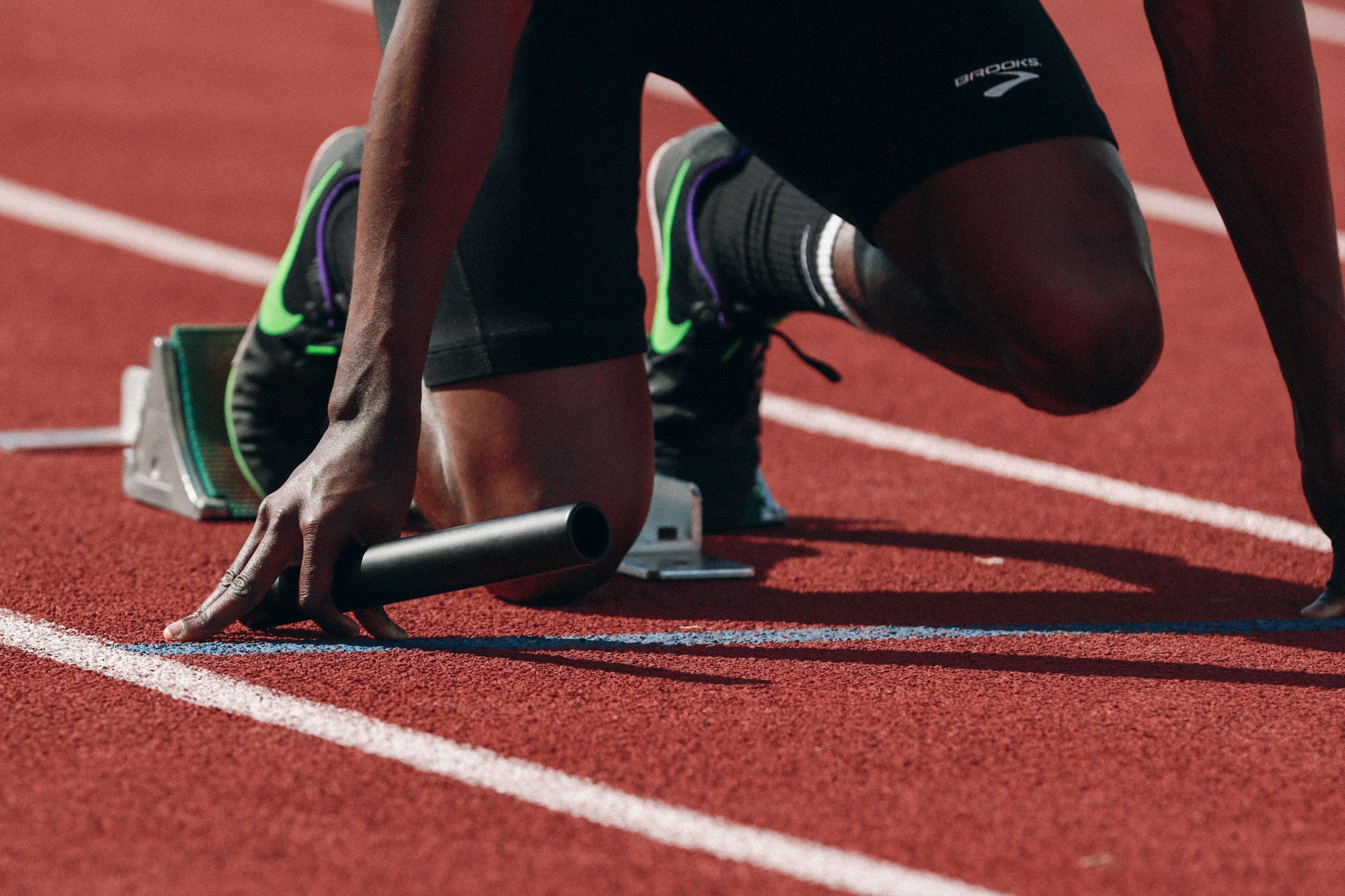 Sprinter in the starting blocks holding a relay baton on a red running track