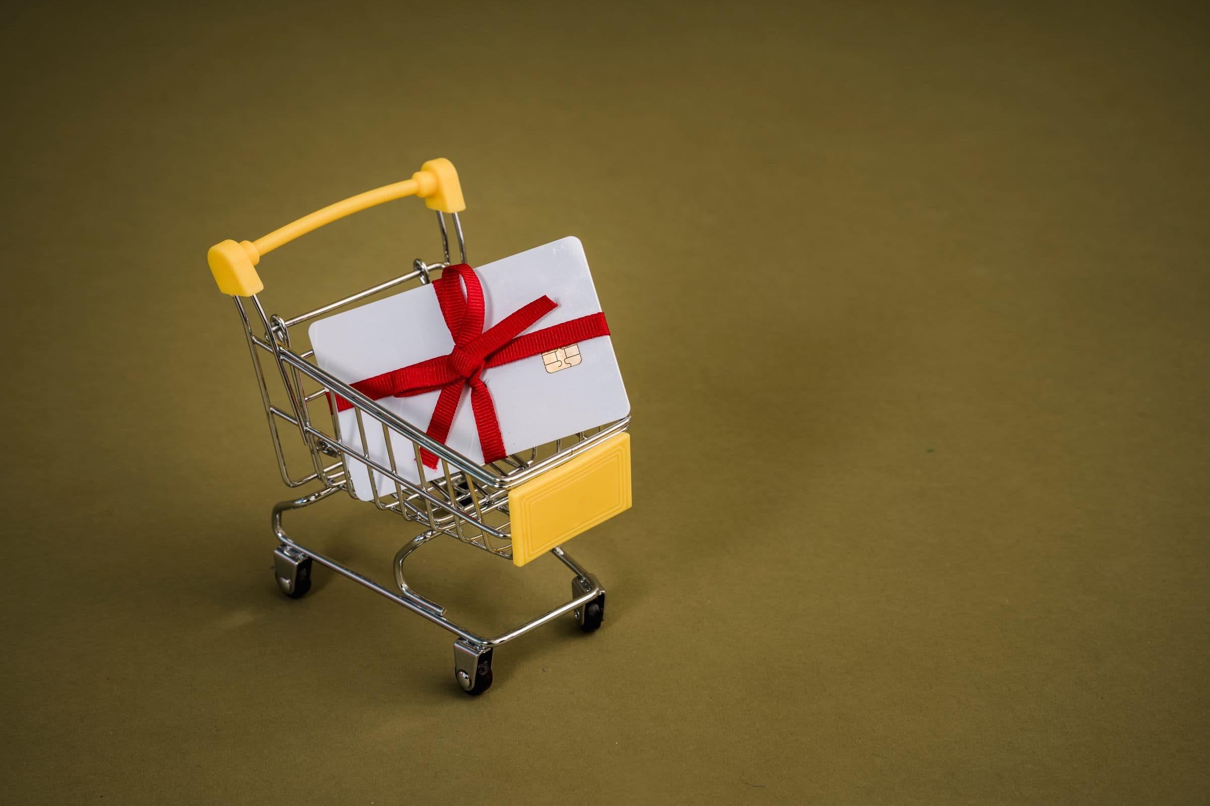 A gift card tied with a red ribbon in a miniature shopping cart
