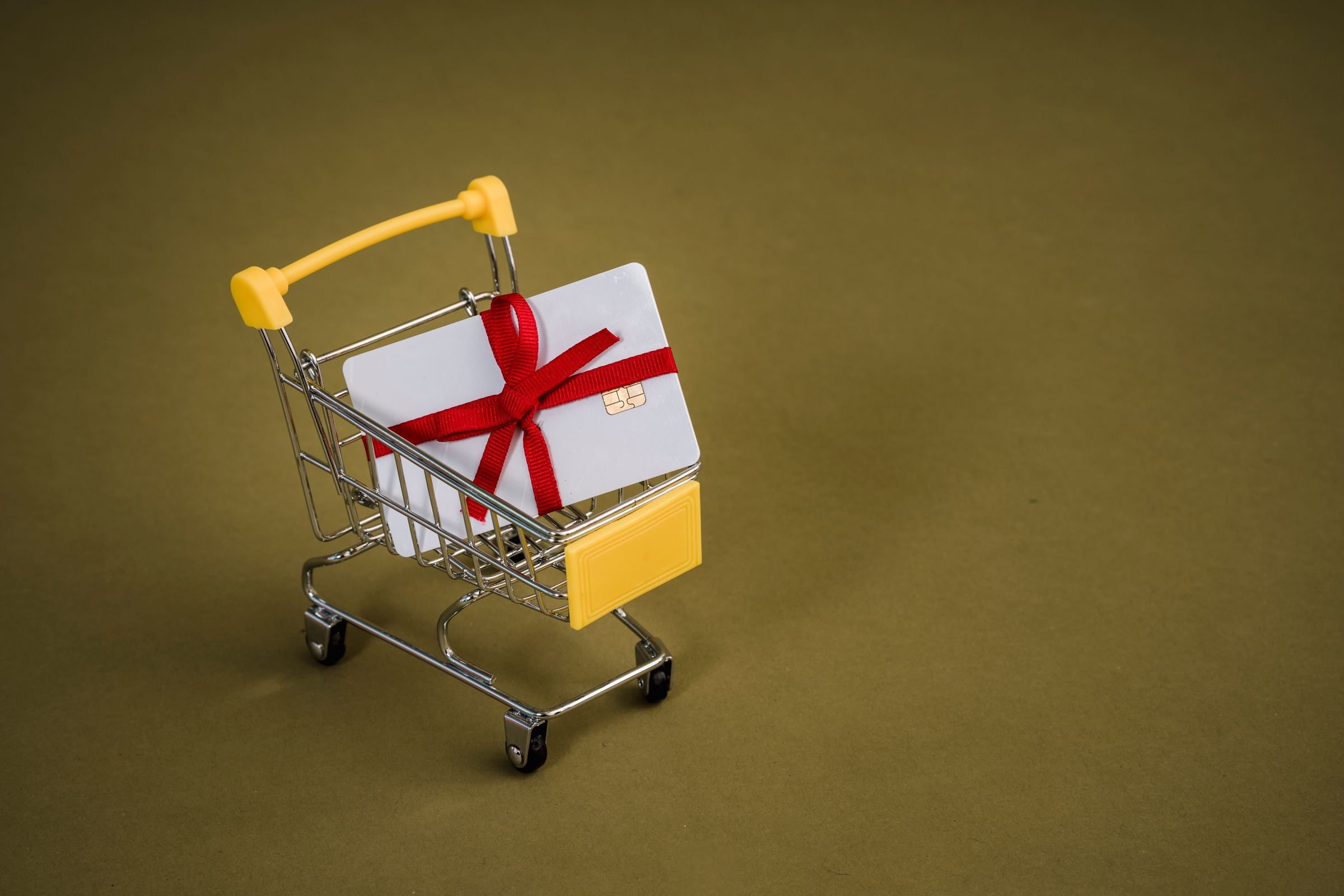 A gift card tied with a red ribbon in a miniature shopping cart