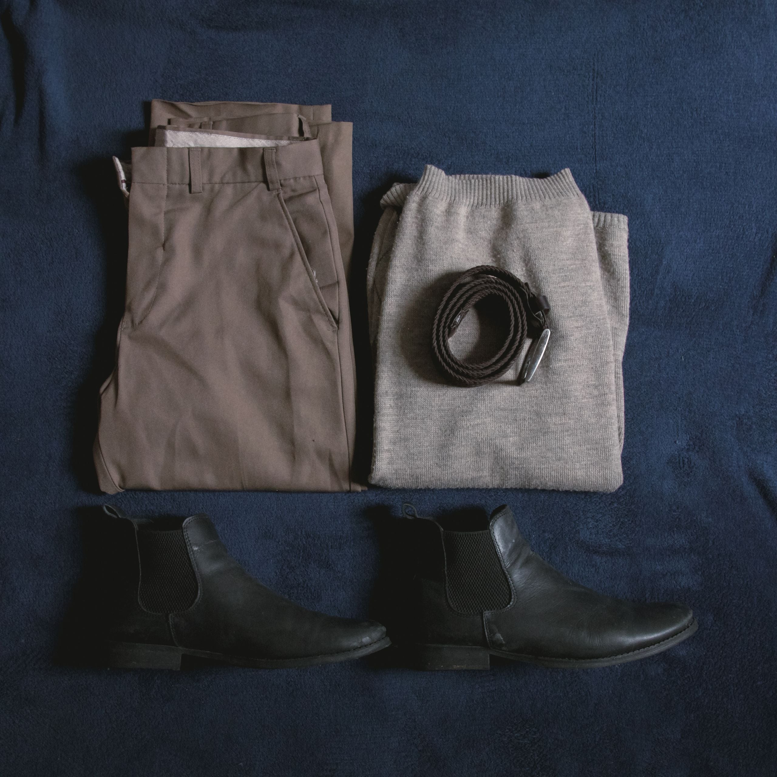Chinos, a knitted jumper, belt and boots laid out on navy