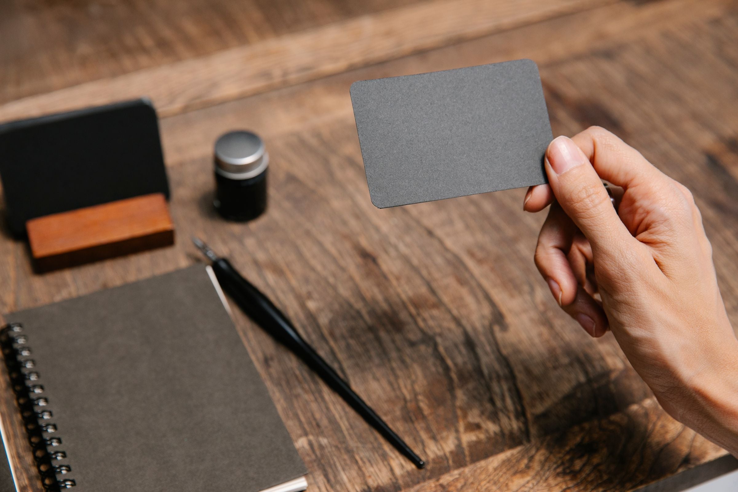 A hand holding a business card over a desk with stationery
